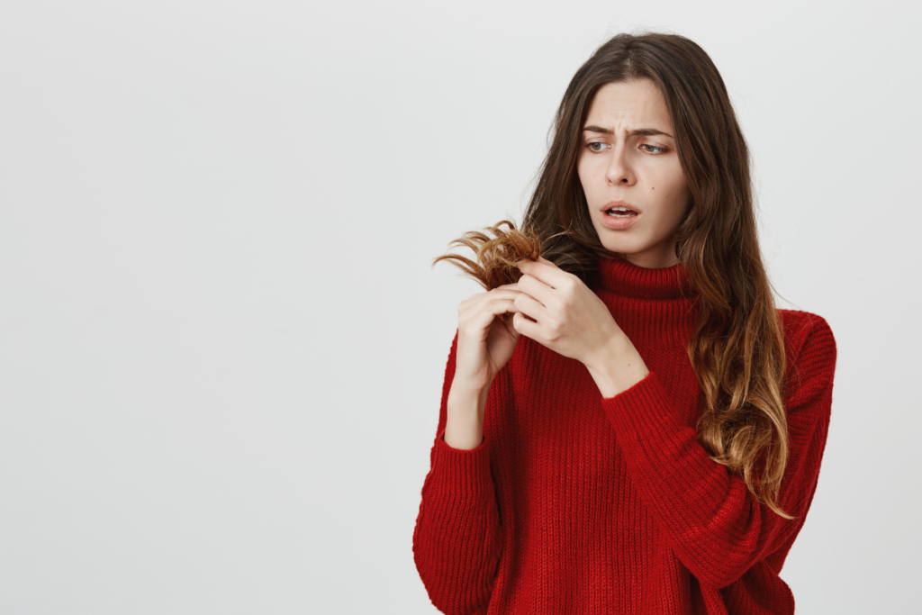 Woman in a red sweater inspecting her hair for split ends, seeking solutions for split ends.