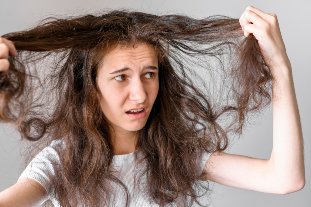 Young woman with frizzy hair looking frustrated, holding tangled strands of her hair. Discover effective tips for frizzy hair.