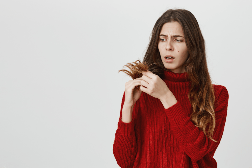 Worried woman in red sweater examining split ends, illustrating common hair care myths debunked.