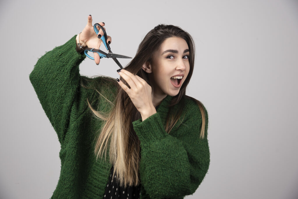Smiling woman in green sweater cutting long hair, representing common Hair Care Myths busted.